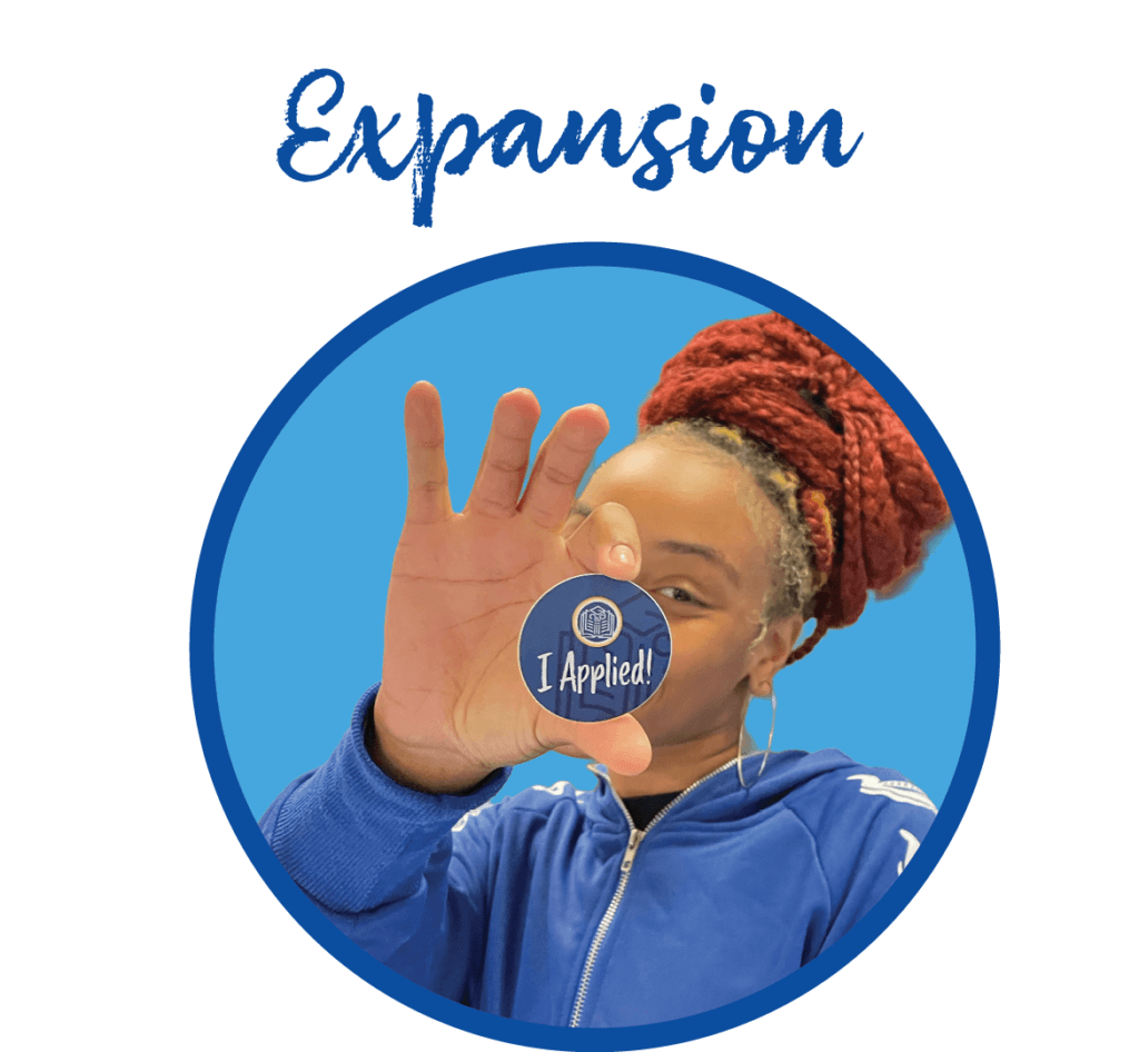 Person in blue jacket holds up a circular pin with the text I Applied! in front of their face. The word Expansion is written above the image.
