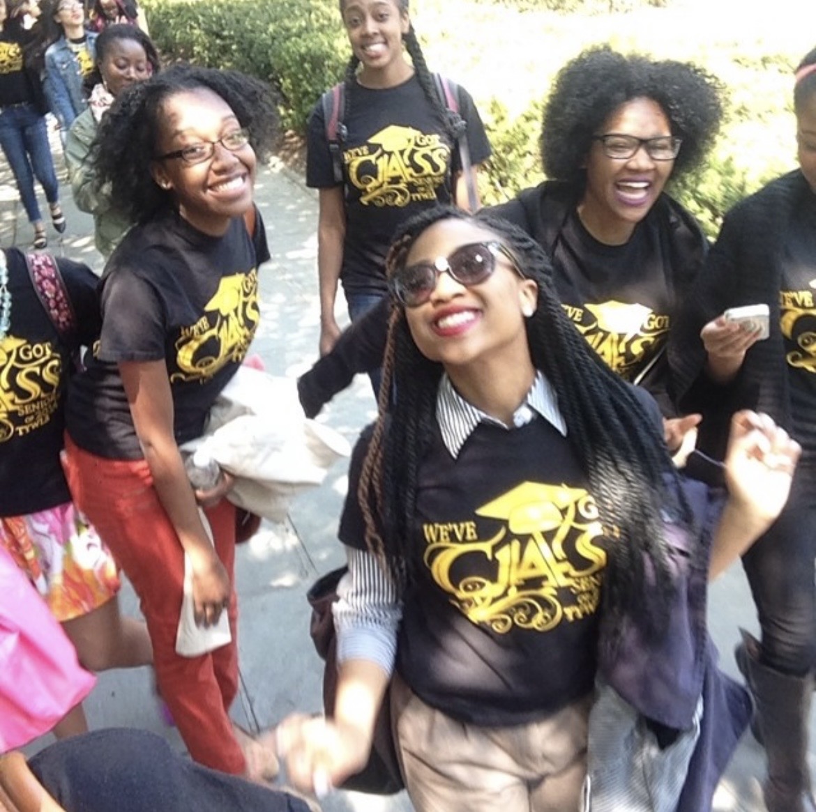 A group of young women wearing matching black shirts with Class of 12 printed on them, smiling and walking outdoors.
